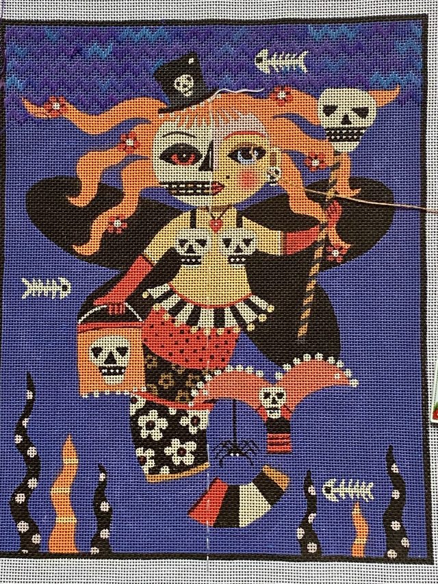 Needlepoint artwork of a Halloween-themed creature with a fish tail and black wings.