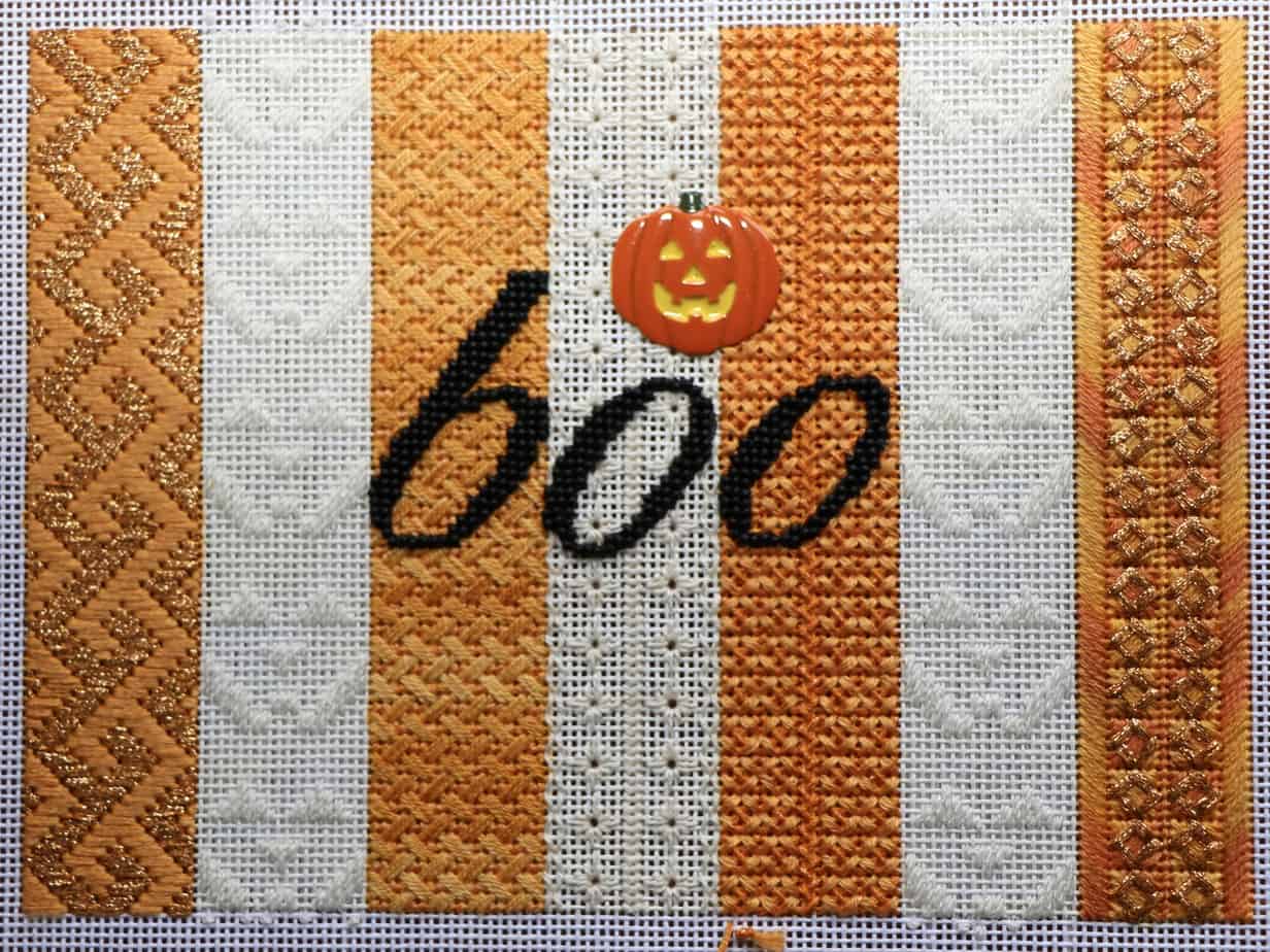 Needlepoint artwork, halloween themed. The word "boo" with a Jack-o'-lantern on top.
