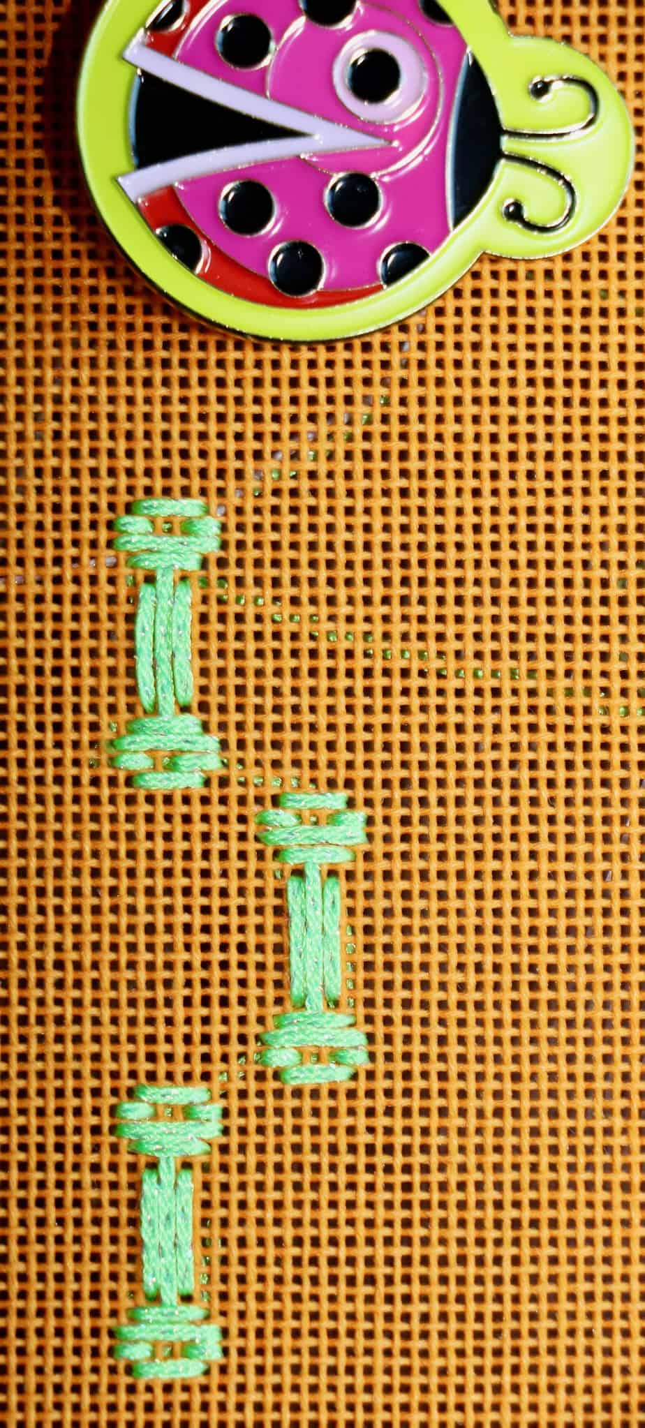 Bones stitched into orange needlepoint canvas, ladybug magnet on the upper side of the photo.